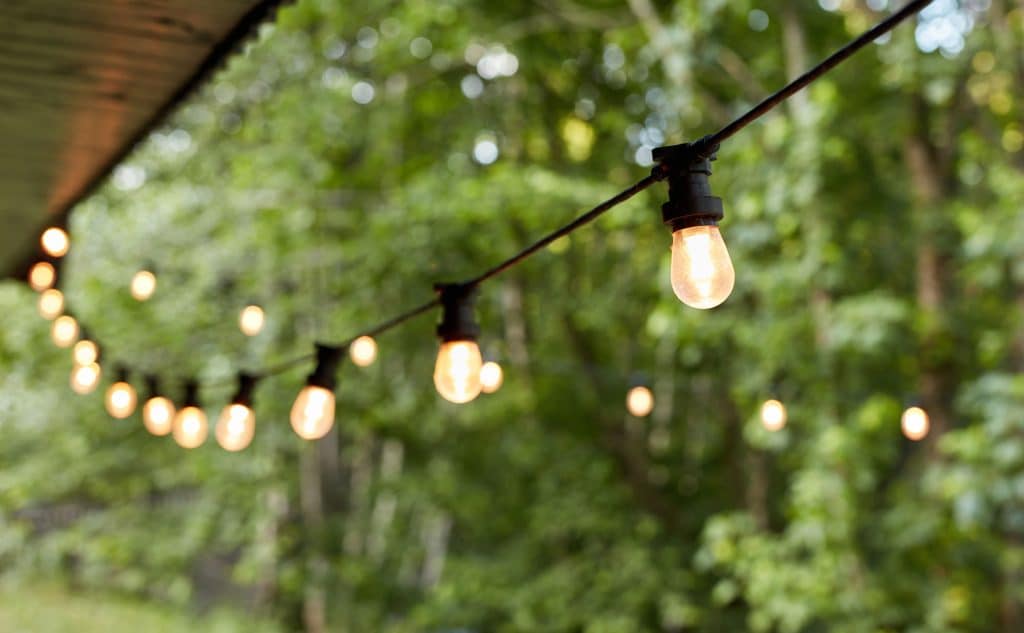 Cafe lighting with warm string lights hanging outdoors by Landscape Lighting Resources in Charlotte NC